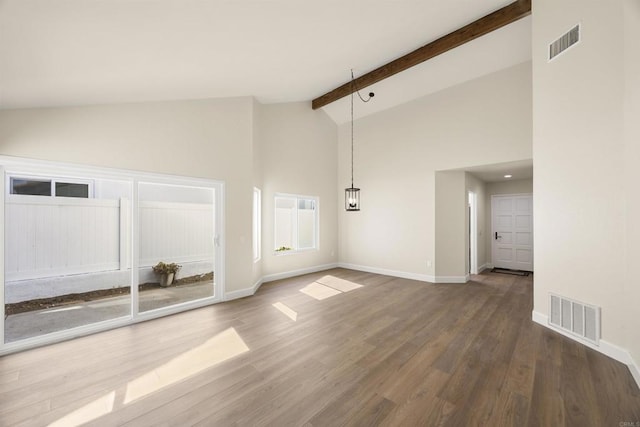 empty room with baseboards, visible vents, beamed ceiling, and wood finished floors