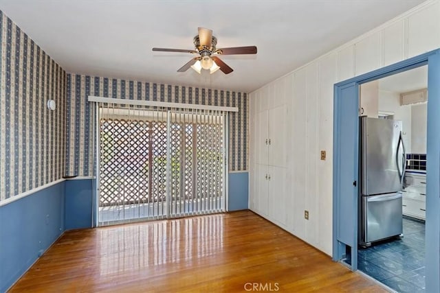 empty room with wallpapered walls, a ceiling fan, and wood finished floors