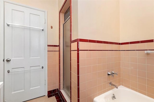 full bath with a wainscoted wall, a garden tub, tile patterned flooring, a shower stall, and tile walls