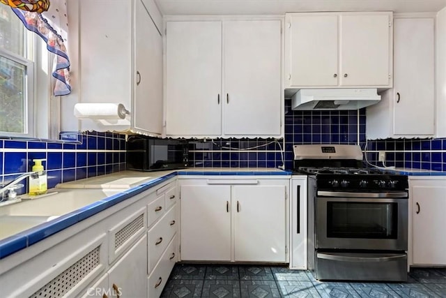 kitchen with under cabinet range hood, stainless steel gas range, white cabinets, and backsplash