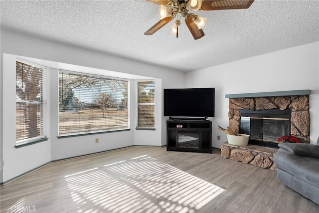 living area featuring a ceiling fan, light wood-type flooring, a fireplace, and a textured ceiling