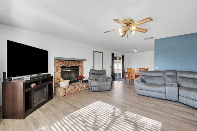 living area with visible vents, ceiling fan, a textured ceiling, light wood-type flooring, and a fireplace