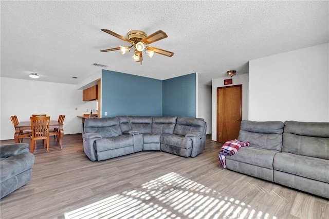 living room featuring ceiling fan, light wood finished floors, a textured ceiling, and visible vents