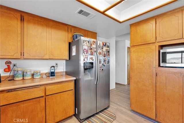 kitchen featuring stainless steel appliances, light countertops, visible vents, light wood-style flooring, and brown cabinetry