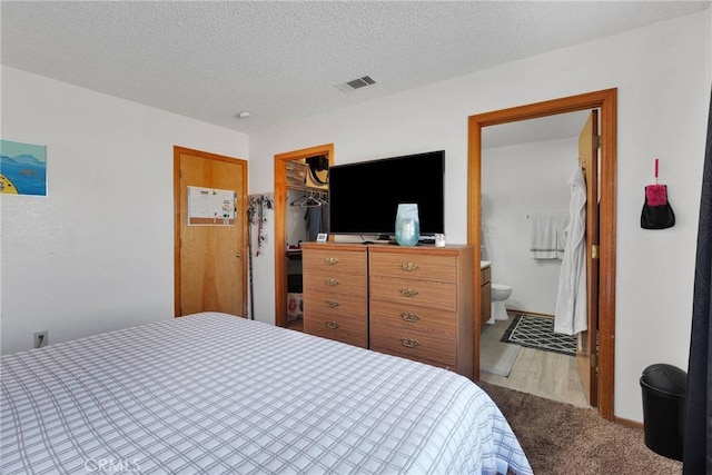 bedroom with a textured ceiling, connected bathroom, visible vents, a closet, and a walk in closet