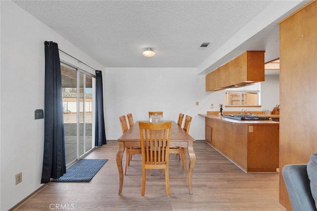 dining space with light wood-type flooring, visible vents, and a textured ceiling