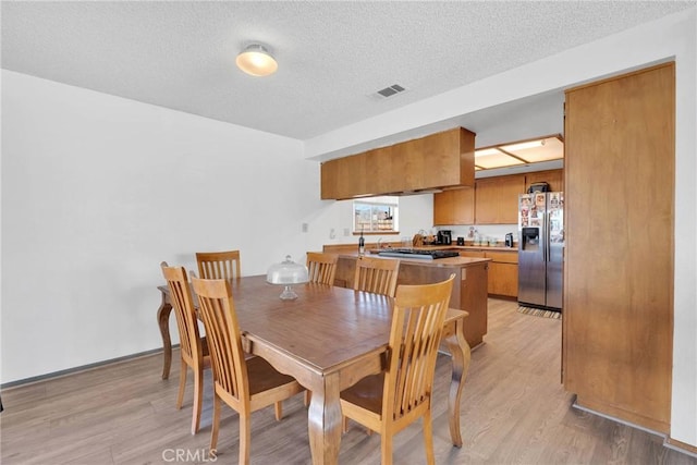 dining space featuring a textured ceiling, visible vents, and light wood-style floors