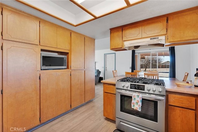 kitchen with light wood finished floors, stainless steel appliances, light countertops, brown cabinetry, and under cabinet range hood