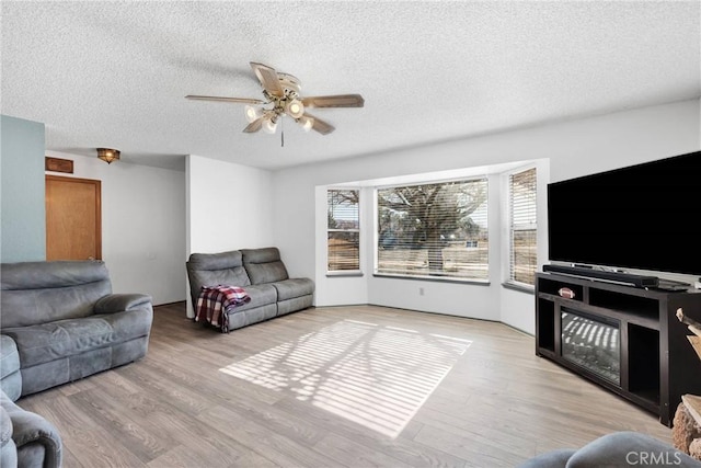 living area with light wood finished floors, ceiling fan, and a textured ceiling