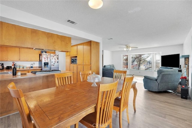 dining room featuring light wood-type flooring, visible vents, ceiling fan, and a textured ceiling