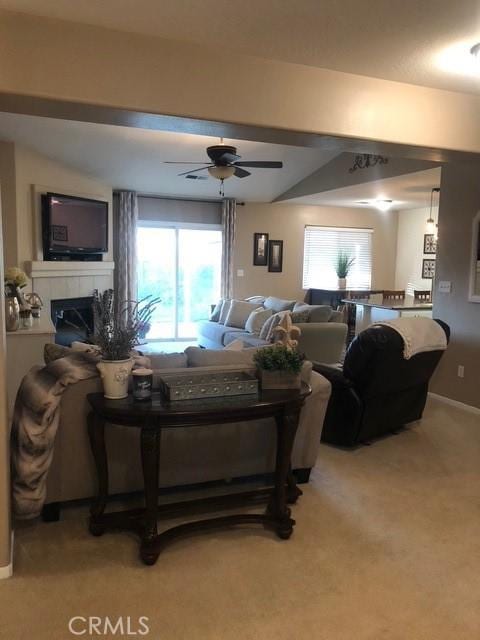 living area featuring ceiling fan, a fireplace, baseboards, and light colored carpet