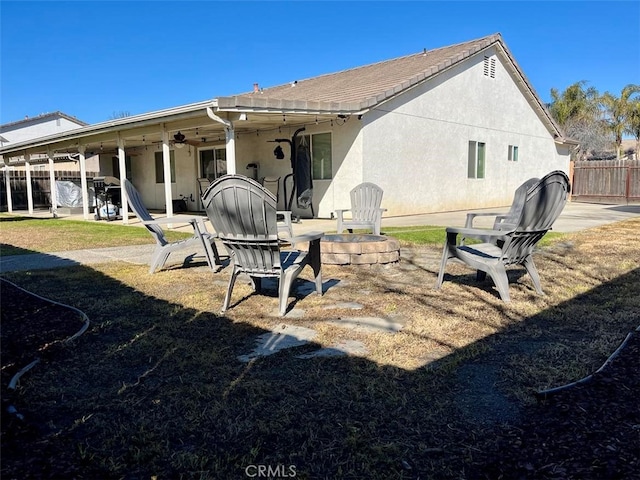 rear view of property featuring an outdoor fire pit, a patio area, fence, and stucco siding