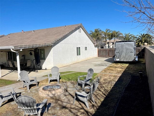 back of property with a fire pit, a patio area, fence, and stucco siding