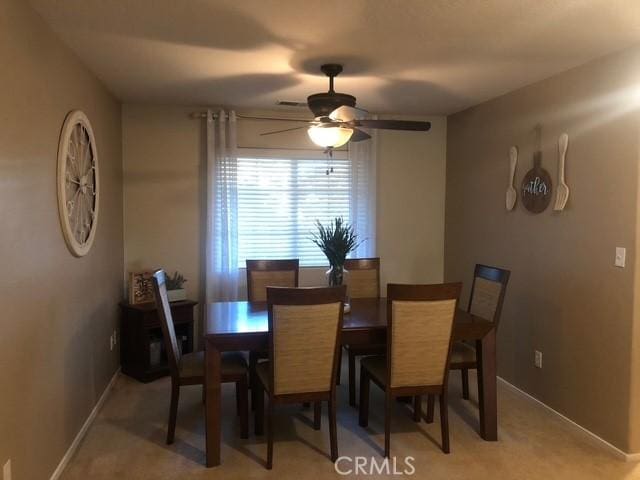 dining area featuring a ceiling fan, light colored carpet, and baseboards