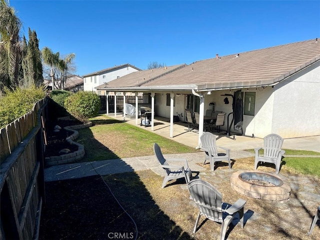 rear view of property with a tile roof, stucco siding, an outdoor fire pit, a patio area, and a fenced backyard