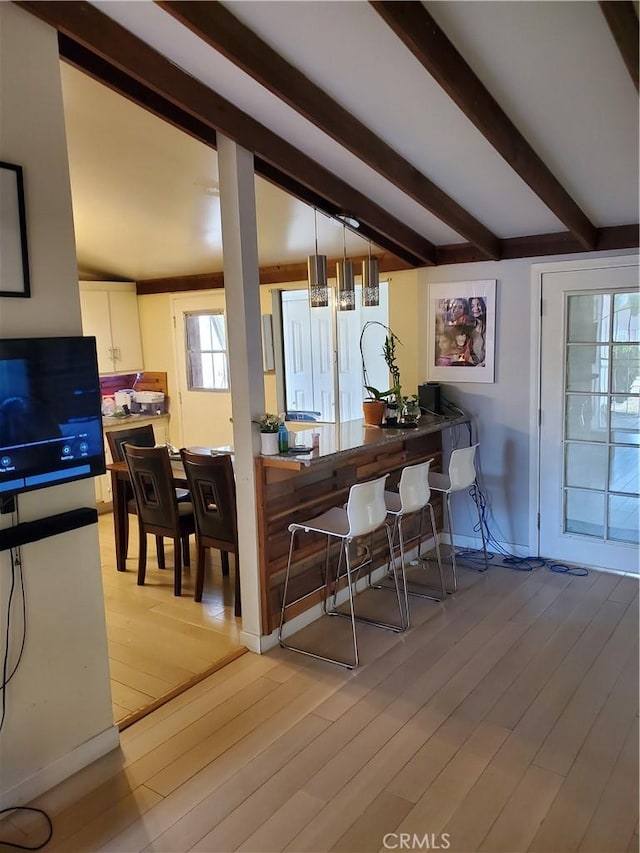 dining area with beamed ceiling, baseboards, and light wood finished floors