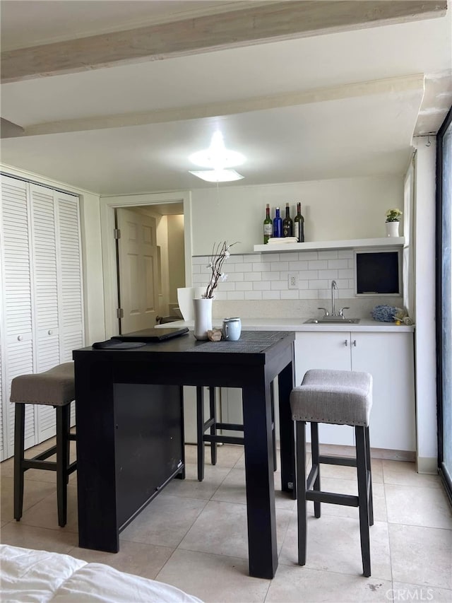 interior space with indoor wet bar, decorative backsplash, light tile patterned flooring, and a sink