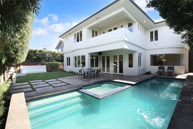 rear view of property with a yard, stucco siding, a pool with connected hot tub, a patio area, and fence