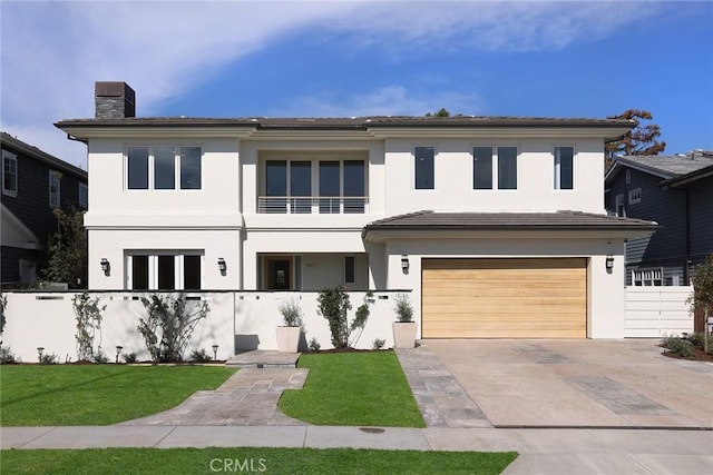 view of front facade with concrete driveway, a chimney, an attached garage, a front lawn, and stucco siding