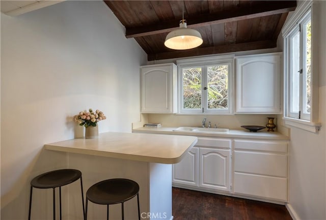 kitchen featuring a breakfast bar area, a peninsula, a sink, white cabinets, and light countertops