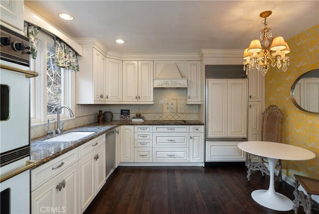 kitchen featuring wallpapered walls, decorative light fixtures, custom exhaust hood, white cabinetry, and a sink