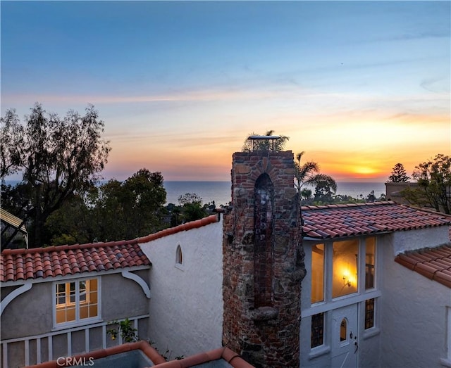 exterior space featuring a tiled roof, a chimney, a water view, and stucco siding