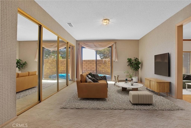 carpeted living room featuring wallpapered walls, visible vents, and a textured ceiling