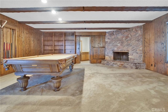 recreation room with a stone fireplace, light colored carpet, wooden walls, and beam ceiling