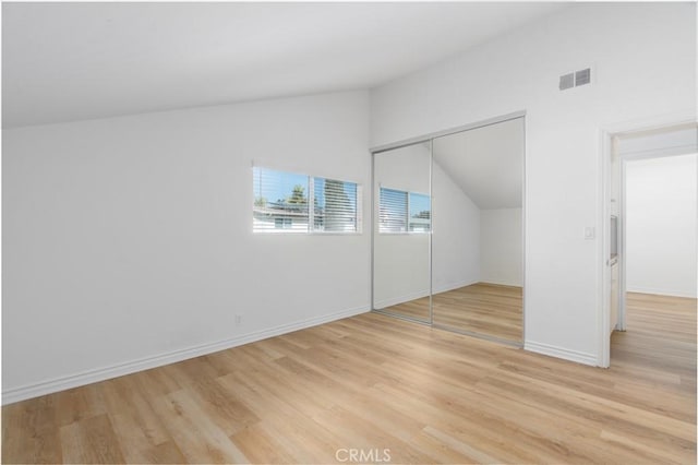 unfurnished bedroom featuring light wood-type flooring, baseboards, visible vents, and vaulted ceiling