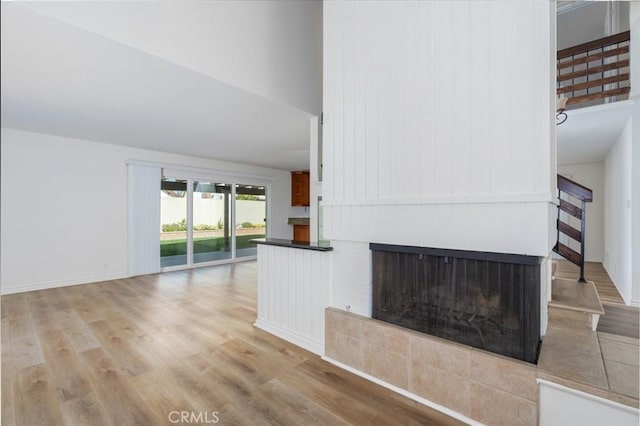 unfurnished living room featuring light wood-type flooring, baseboards, a multi sided fireplace, and stairs