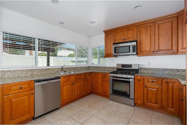 kitchen with brown cabinets, appliances with stainless steel finishes, light stone counters, and a sink