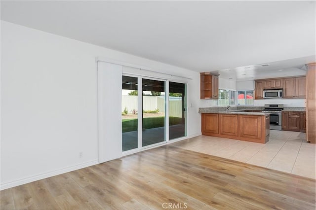 kitchen with appliances with stainless steel finishes, brown cabinets, a peninsula, light countertops, and open shelves