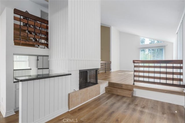 unfurnished living room with vaulted ceiling, a multi sided fireplace, and wood finished floors