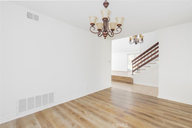 empty room featuring stairs, visible vents, light wood-style flooring, and an inviting chandelier