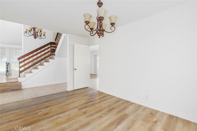 unfurnished dining area with a chandelier, wood finished floors, stairs, and baseboards