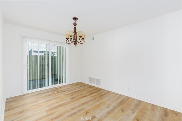 unfurnished room featuring baseboards, visible vents, an inviting chandelier, and wood finished floors