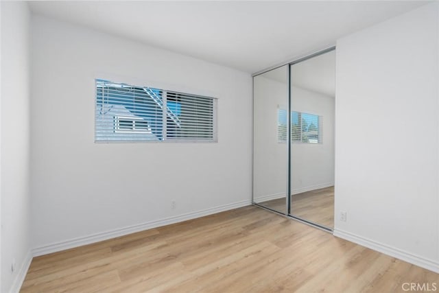 unfurnished bedroom featuring light wood finished floors, a closet, and baseboards