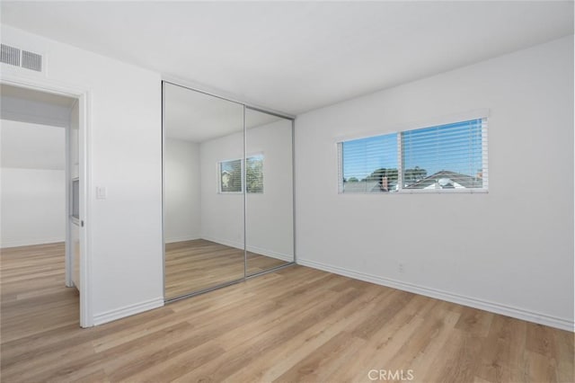 unfurnished bedroom featuring baseboards, light wood-style flooring, visible vents, and a closet