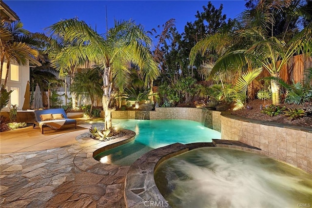 pool at night with a patio area, fence, an outdoor pool, and an in ground hot tub