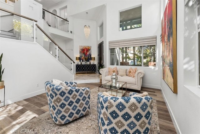 living area featuring a towering ceiling, stairway, baseboards, and wood finished floors