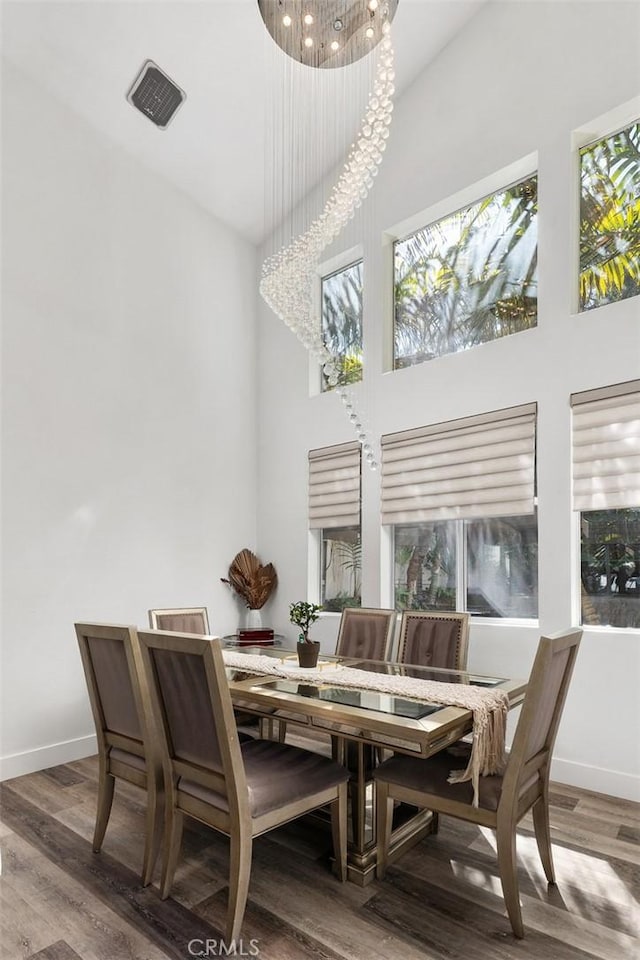 dining area with baseboards, a high ceiling, visible vents, and wood finished floors