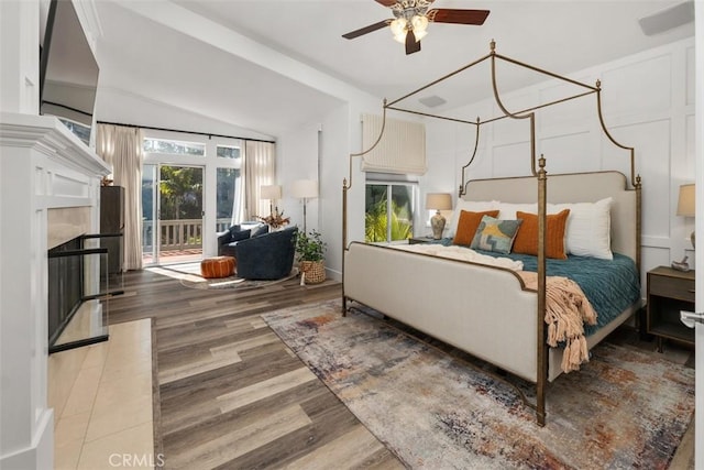 bedroom featuring access to exterior, a fireplace, vaulted ceiling, and wood finished floors