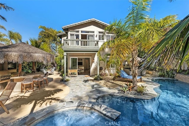 rear view of house with stucco siding, an outdoor kitchen, a balcony, exterior bar, and an outdoor pool