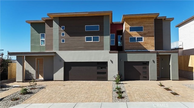 contemporary home with a garage, driveway, fence, and stucco siding