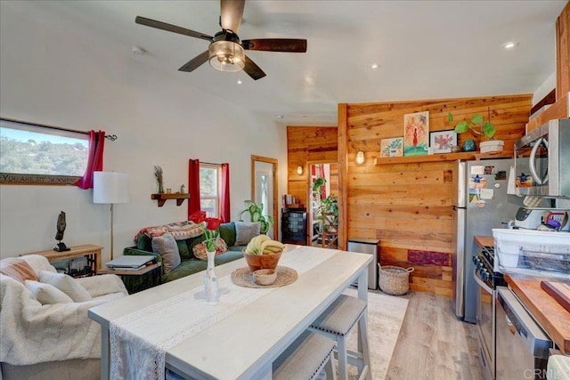 kitchen featuring stainless steel appliances, ceiling fan, light wood-style flooring, wood walls, and open floor plan