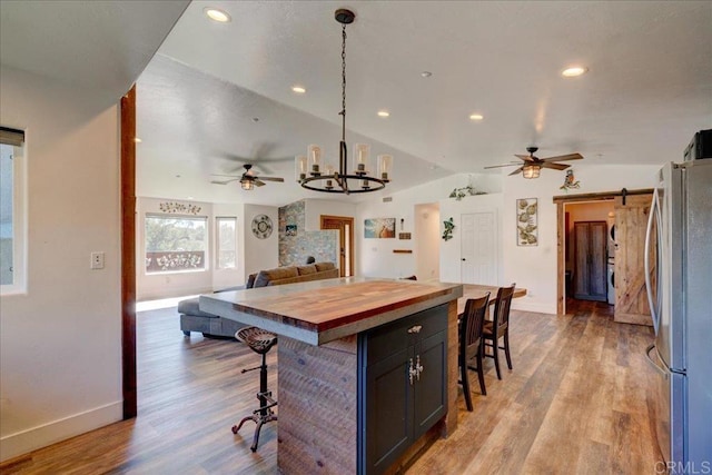kitchen with wood counters, a kitchen breakfast bar, freestanding refrigerator, and ceiling fan with notable chandelier