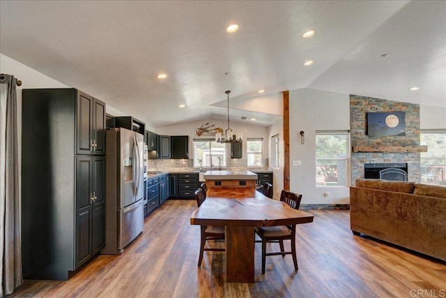 dining room with recessed lighting, an inviting chandelier, lofted ceiling, a stone fireplace, and wood finished floors