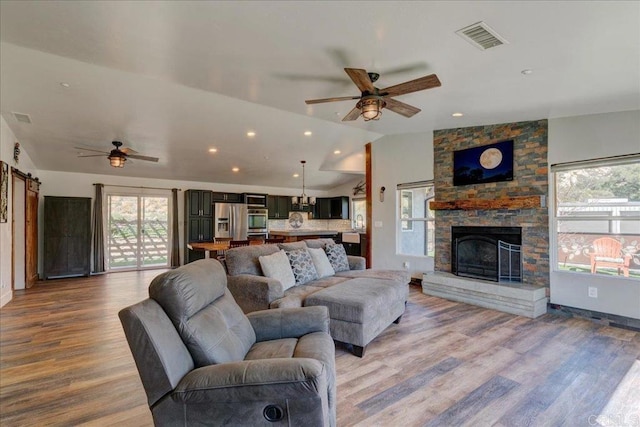 living area featuring a fireplace, light wood-style floors, ceiling fan, visible vents, and vaulted ceiling