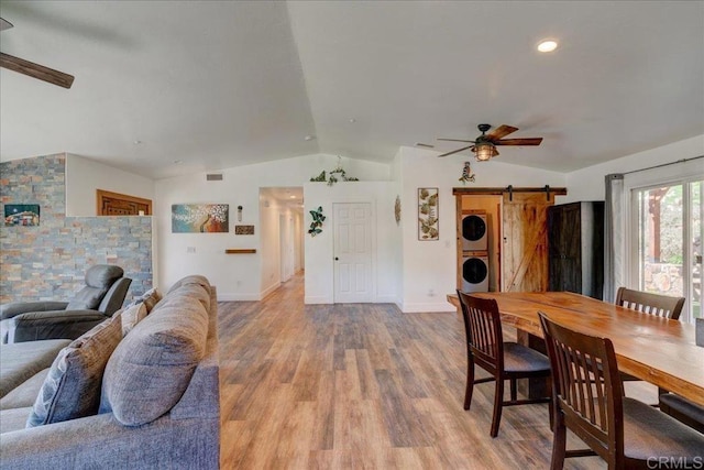 dining space featuring stacked washer and dryer, ceiling fan, vaulted ceiling, and a barn door