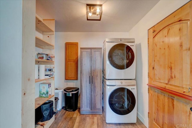 clothes washing area with stacked washer / drying machine, cabinet space, and light wood-style flooring